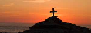Cruz en una colina y un atardecer de fondo.