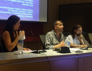 Tres personas sentadas en la mesa principal de un auditorio.
