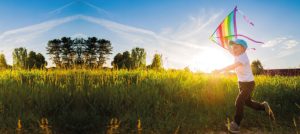 Niño elevando una cometa en un campo abierto.