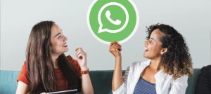 Dos mujeres hablando. Una de ellas sostiene un ícono de la aplicación WhatsApp.