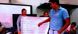 Mujer sostiene una cartelera y un hombre hace una exposición de los temas ahí escritos.