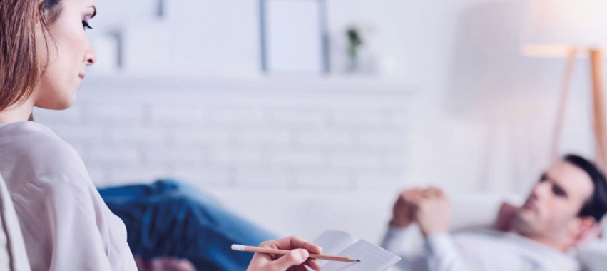 Psicóloga atiende a paciente que se encuentra acostado en un sofá.