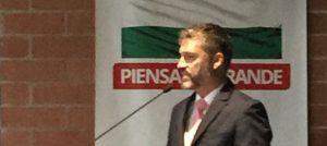 Hombre al frente de un micrófono. Al fondo, bandera del departamento de Antioquia.