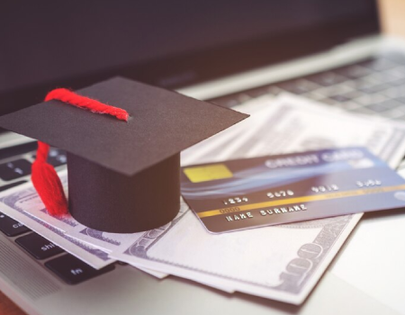 Birrete, tarjeta de cédito y dinero sobre el teclado de un computador portátil.