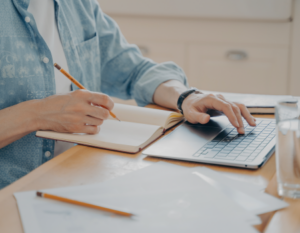 Persona escribiendo con un lápiz e interactuando con un computador portátil.