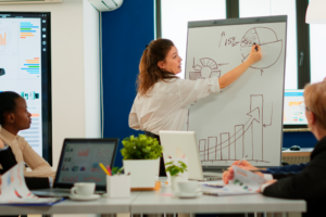 Mujer liderando reunión en el que ella presenta gráficas estadísticas.