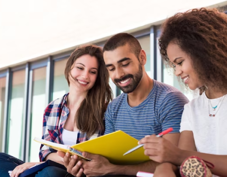 Tres jóvenes universitarios leen de un libro de pasta amarilla.