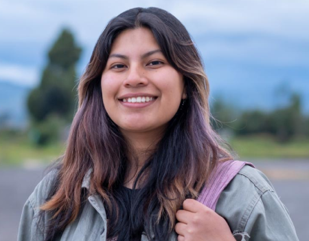 Mujer joven sonriendo a la cámara y sosteniendo un bolso con su mano izquierda.