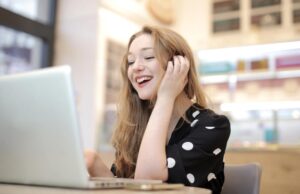 Mujer rubia sonriendo frente a un computador portátil blanco.