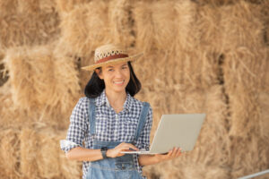 Mujer sosteniendo un computador portátil en medio de un lugar agropecuario.