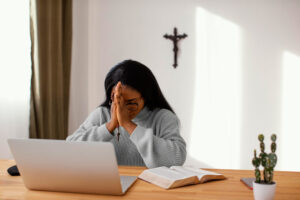 Religiosa orando frente a un computador portátil y de espaldas a un crucifijo.