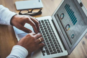 Manos sobre un computator portatil donde seproyectan gráficos estadísticos.