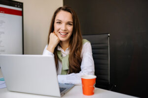 Mujer sentada frente a un computador portátil apoya su cabeza sobre el puño de su mano derecha.