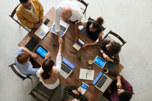 Vista cenital de un grupo de personas trabajando en torno a una mesa donde hay varios computadores portátiles.