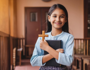Niña sonriente abrazando una Biblia y sosteniendo un crucifijo en sus manos.