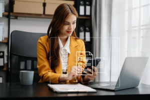 Mujer en un entorno corporativa usa un teléfono celular en frente de un computador portátil.