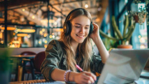 Estudiante en una sesión virtual de clases sentada al frente de su computador portátil y usando unas diademas.