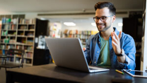 Estudiante en una sesión virtual de clases sentada al frente de su computador portátil y usando unas diademas.