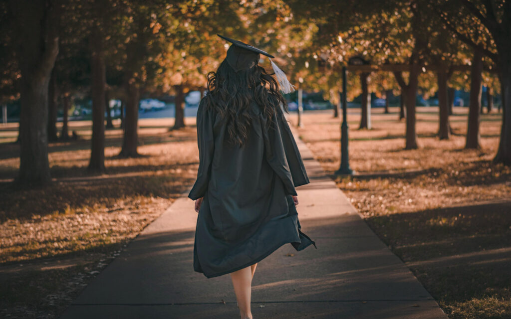 Mujer vestida de graduada caminando entre árboles