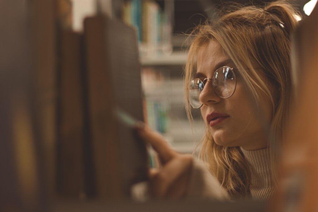 Mujer con lentes buscando libro en biblioteca