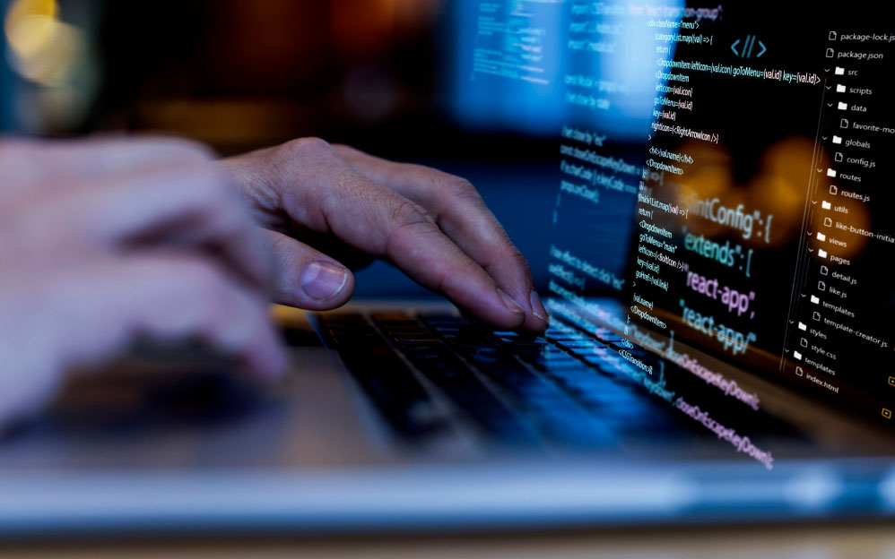 Foto de manos en teclado y pantalla mostrando un trabajo a base de código