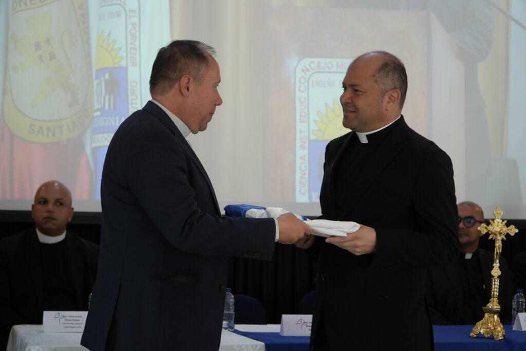 Monseñor Diego Luis Rendón Urrea entrega la bandera institucional al padre Eduin Alberto Salazar, nuevo rector de la Fundación Universitaria Católica del Norte.
