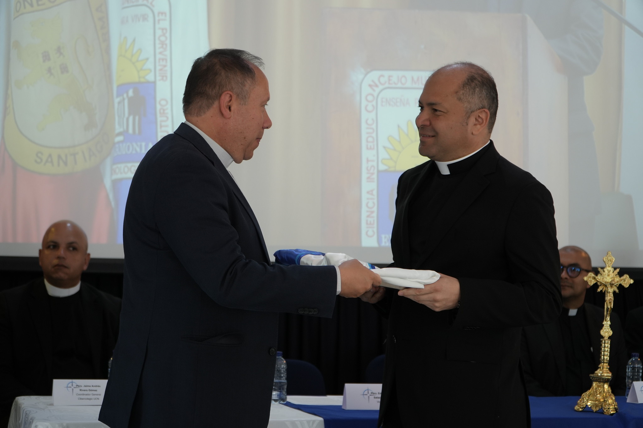 Monseñor Diego Luis Rendón Urrea entrega la bandera institucional al padre Eduin Alberto Salazar, nuevo rector de la Fundación Universitaria Católica del Norte.